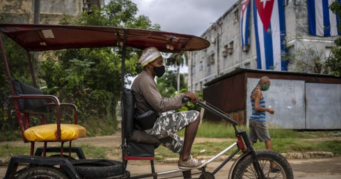 Hombre Conduciendo bicicleta/taxi con bandera de Cuba al fondo en la habana